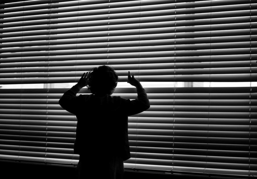 Child looking out of window blinds